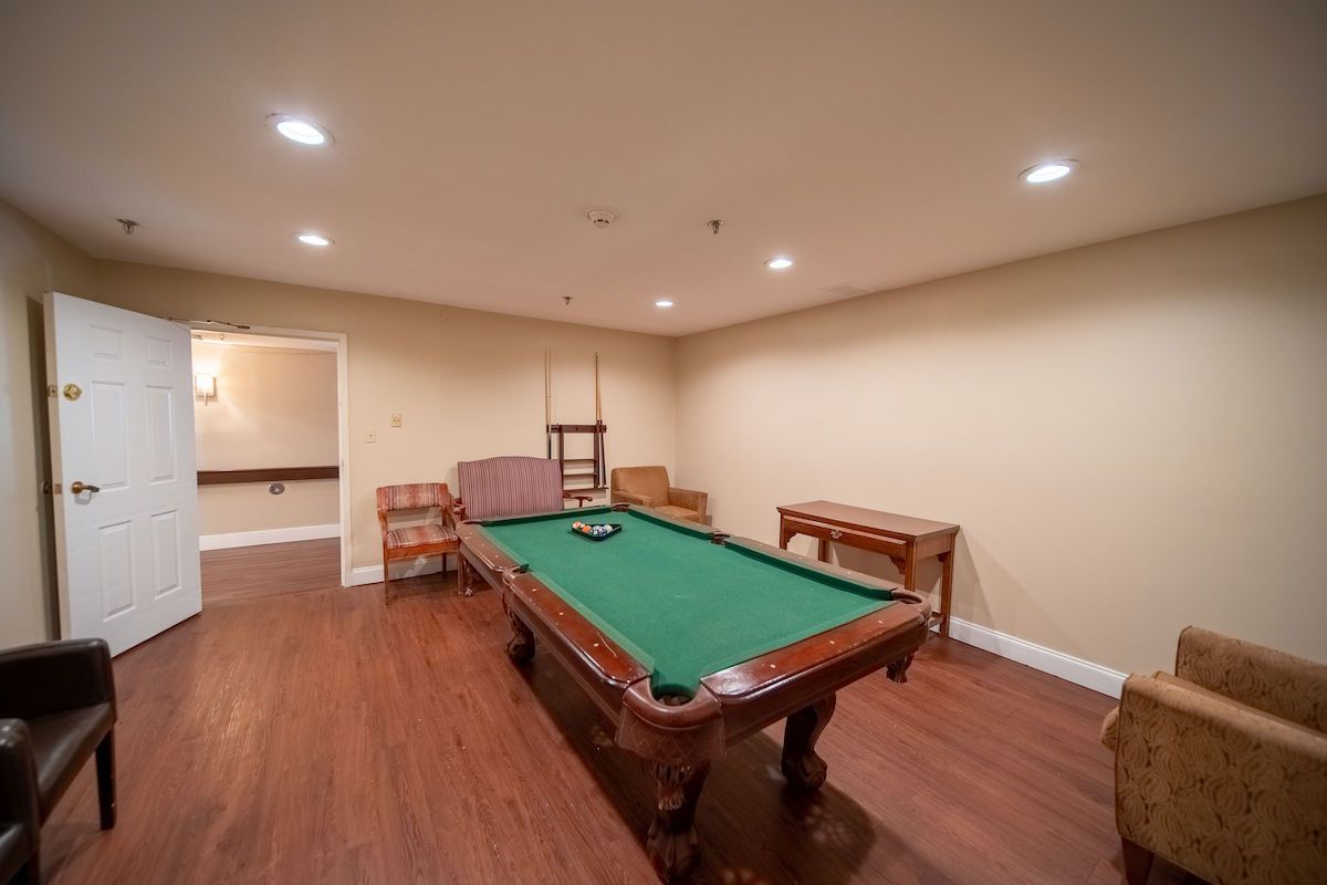 A cozy game room featuring a pool table with green felt, surrounded by wooden furniture and warm lighting.