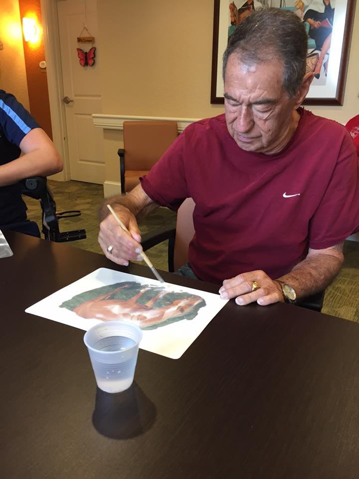 A senior man engaged in painting at a table.