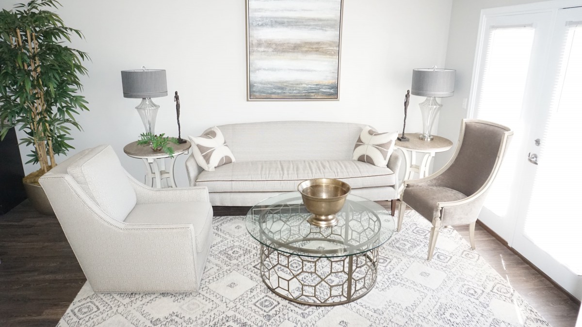 A modern living room with neutral tones featuring a sleek sofa, glass coffee table, and coordinating lamps.