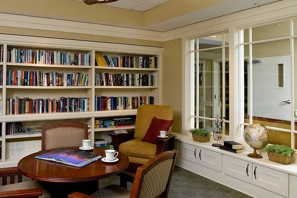 A cozy reading room with bookshelves, an armchair, and a table set for coffee.