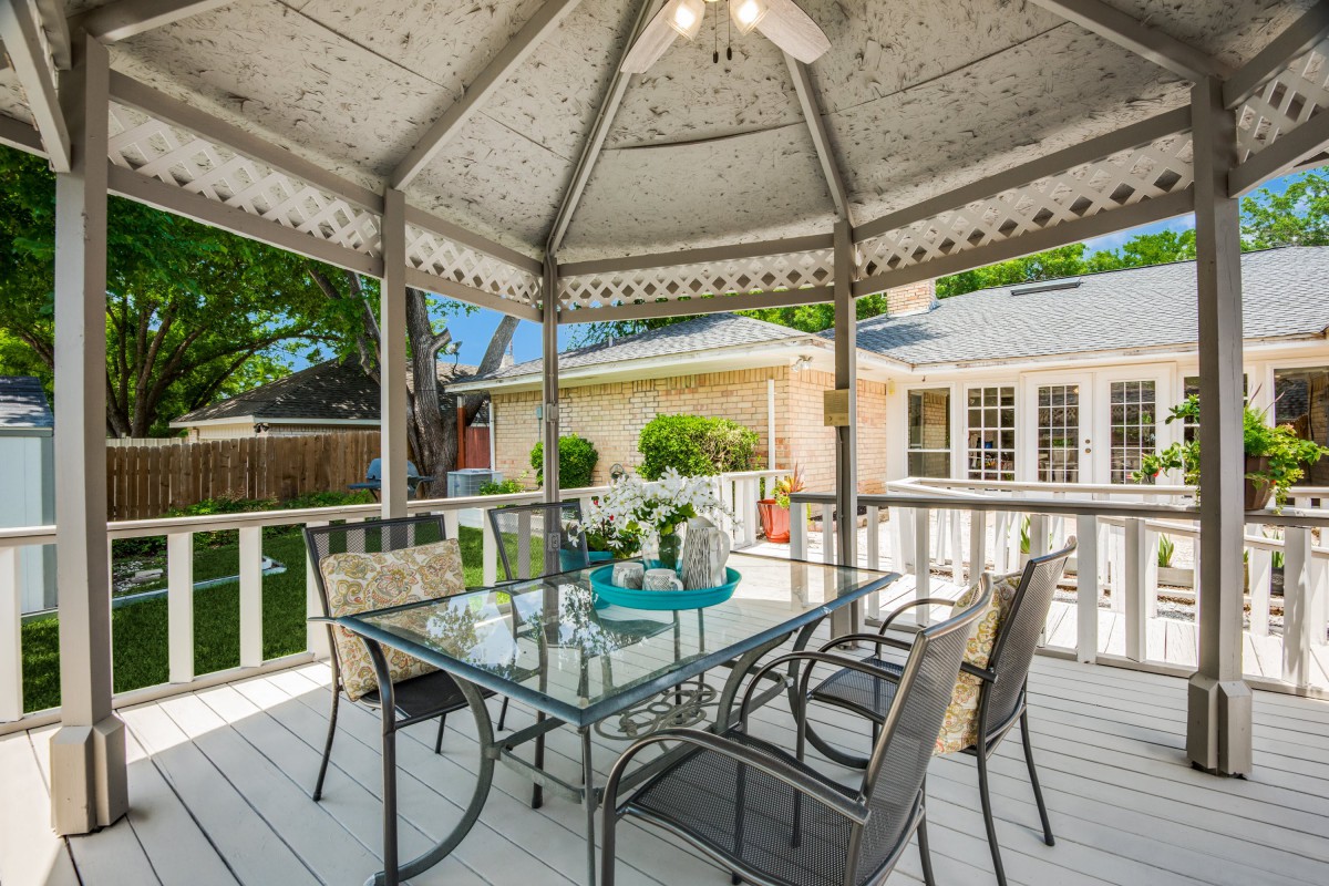 A cozy gazebo with a glass dining table and chairs, nestled in a backyard setting.