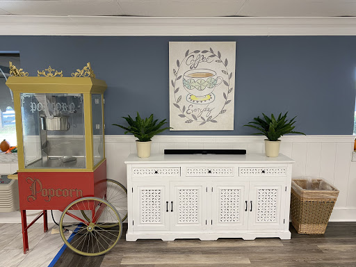 A cozy and stylish interior featuring a white cabinet, botanical artwork, and a vintage popcorn cart against a blue wall.