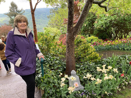 A woman enjoying a serene moment in a lush garden with blooming flowers and a Buddha statue.