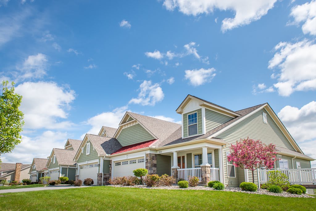 A row of suburban houses with well-maintained lawns under a clear blue sky.
