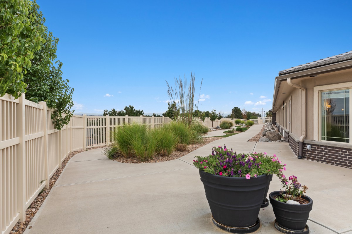 A peaceful outdoor pathway lined with potted plants and a white fence under a clear blue sky.