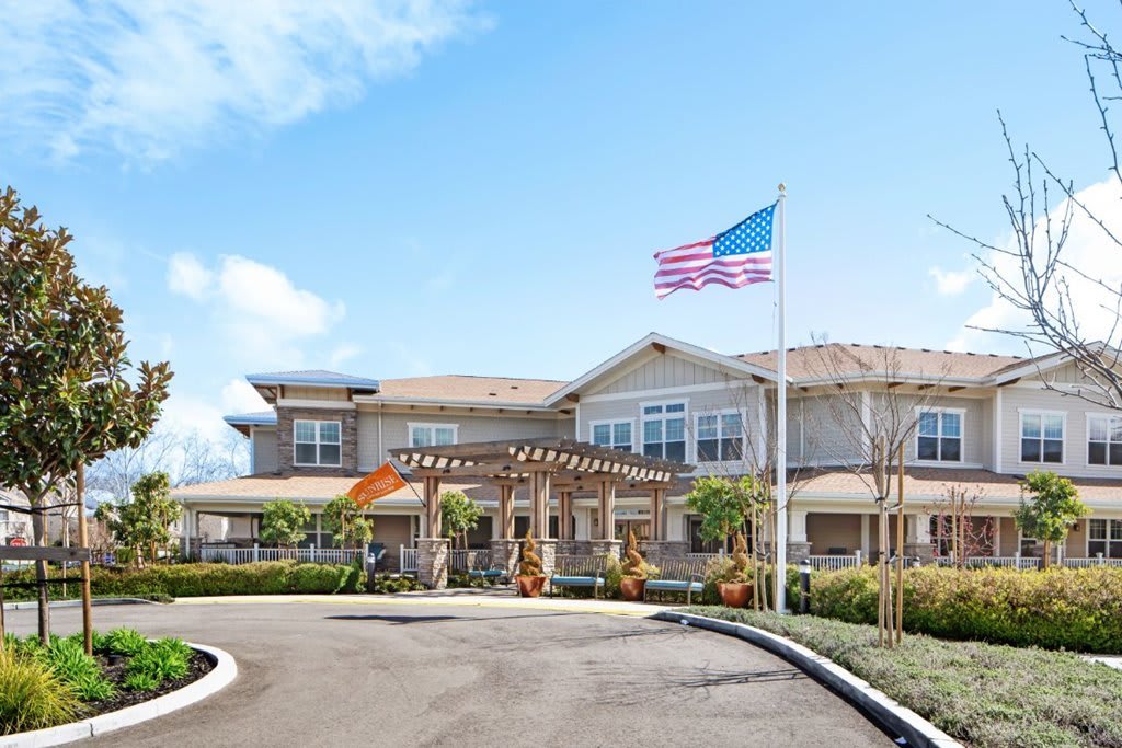 A residential building with an American flag at the entrance surrounded by landscaped greenery.