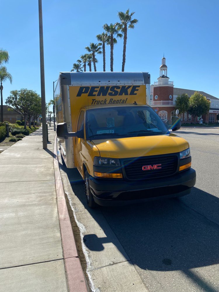 A Penske moving truck parked on a sunny street lined with palm trees.