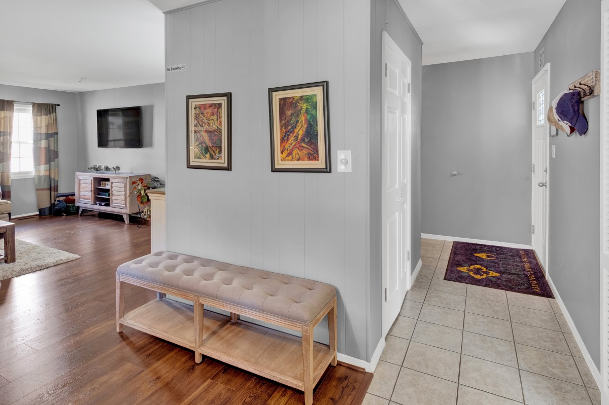 A modern hallway featuring a cushioned bench, two framed artworks on grey walls, and a combination of wooden and tiled flooring.