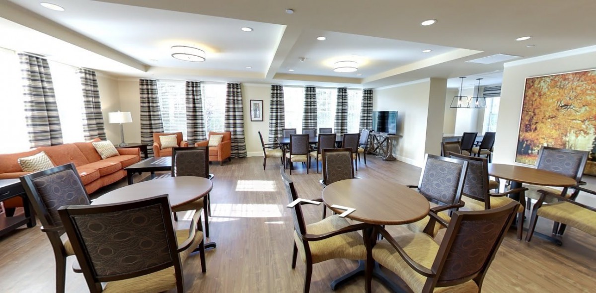 A modern dining area with multiple tables and chairs, featuring large windows with curtains and a TV.