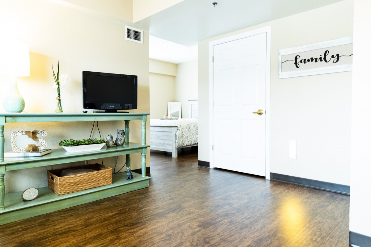 A cozy living space featuring a television on a green shelf, with a view into the adjacent bedroom.