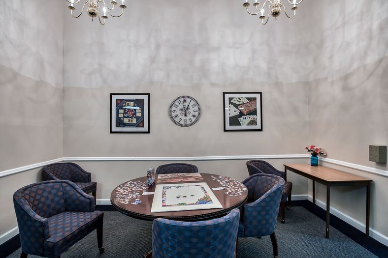 A cozy meeting room with a round table surrounded by chairs, decorated with artwork and a wall clock.