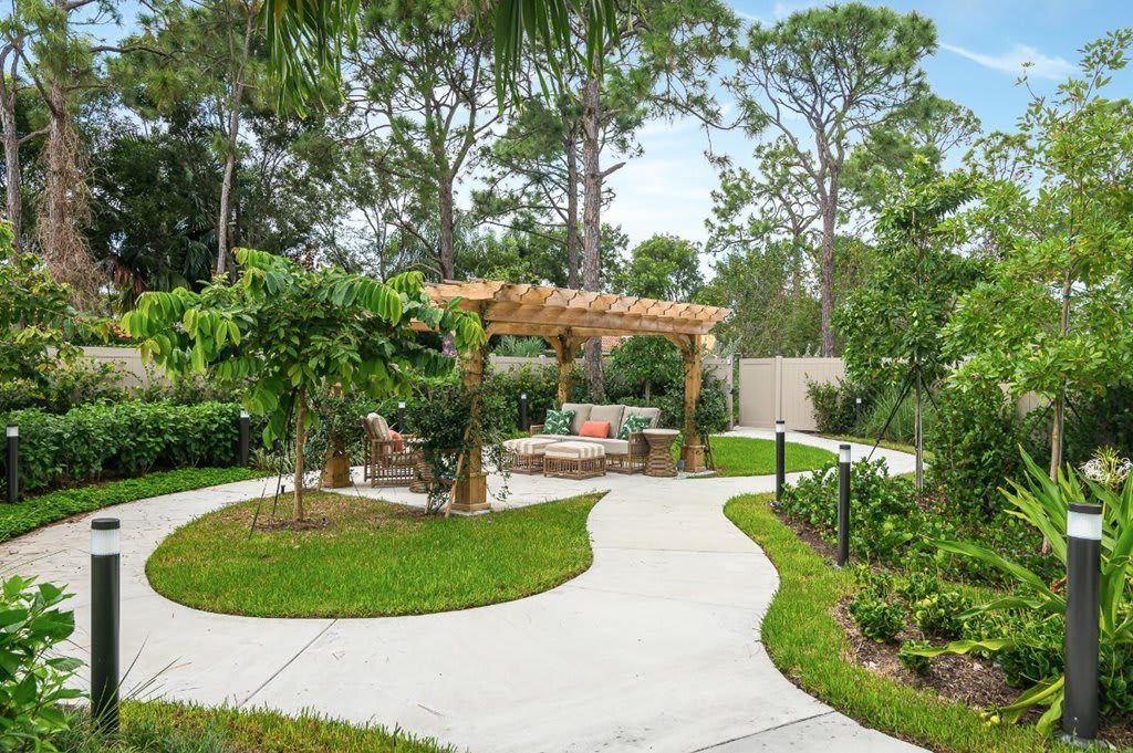 A serene garden with a curved pathway leading to a pergola surrounded by lush greenery.