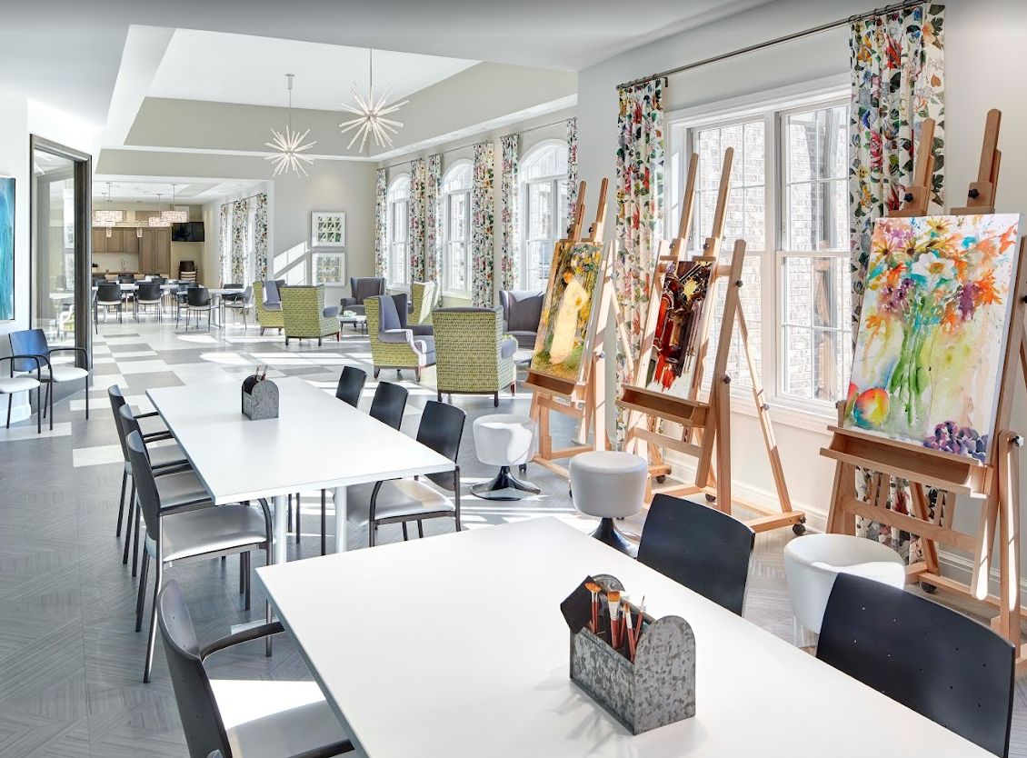 A bright and airy art studio with tables, chairs, and easels set up for painting.