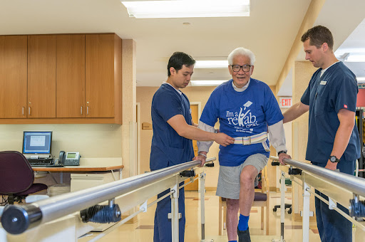 A healthcare professional assists an elderly patient during a physical therapy session in a rehabilitation facility.