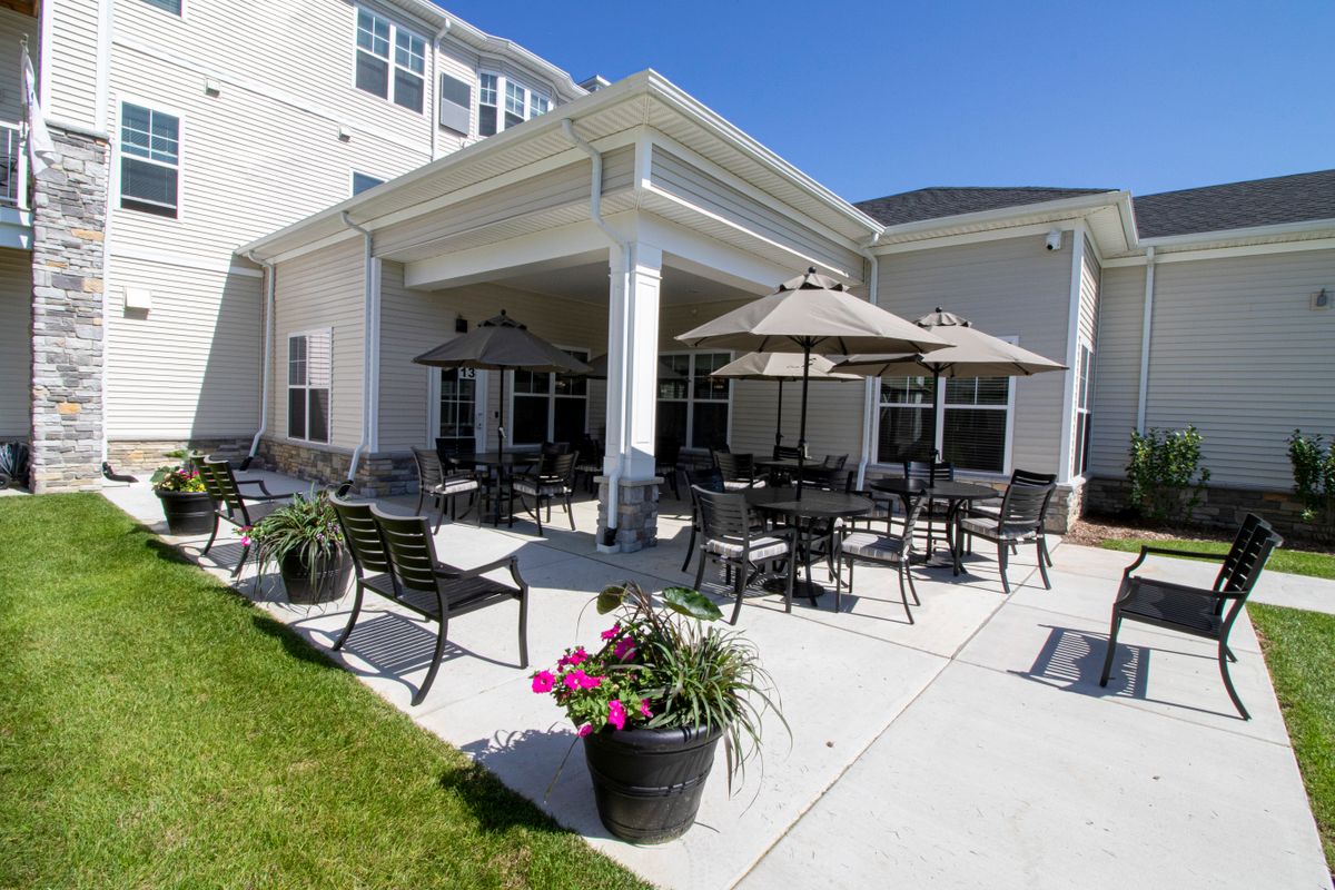 A sunny patio with outdoor seating featuring tables, chairs, umbrellas, and decorative plants.