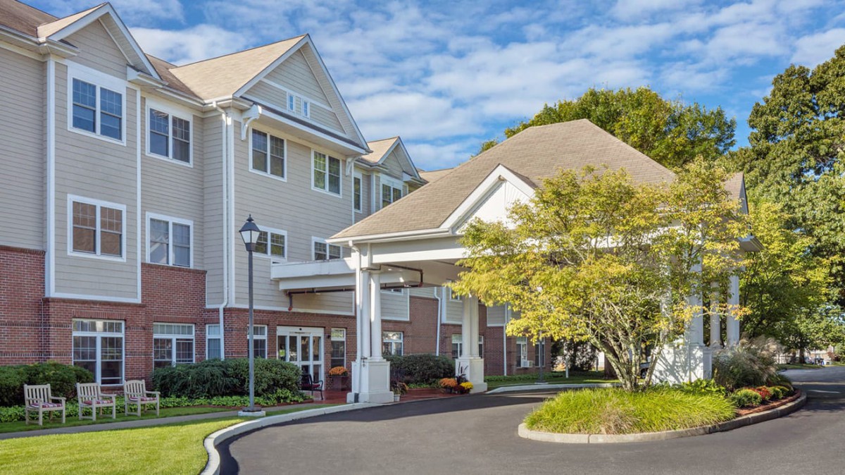 A scenic view of a residential building entrance surrounded by greenery on a clear day.