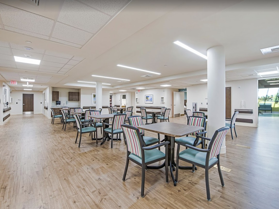 A spacious dining room with multiple tables and chairs, featuring bright lighting and a wooden floor.