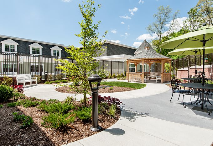 A well-maintained garden with a gazebo and outdoor seating area surrounded by lush greenery and a modern building in the background.