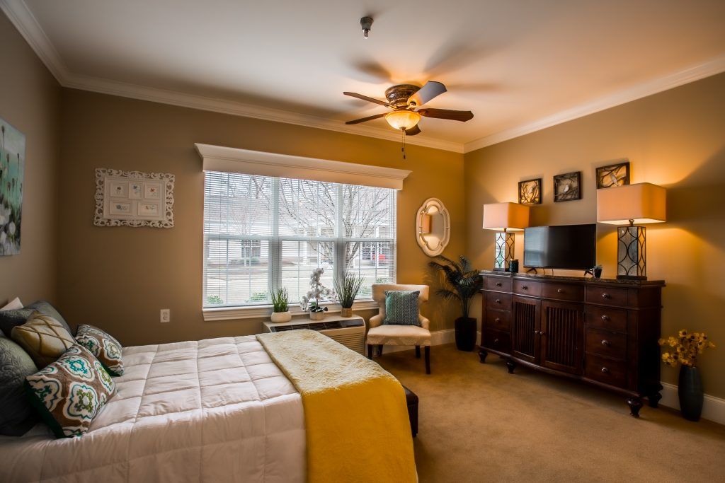 A cozy bedroom with a large window, featuring a bed, dresser, and comfortable seating.