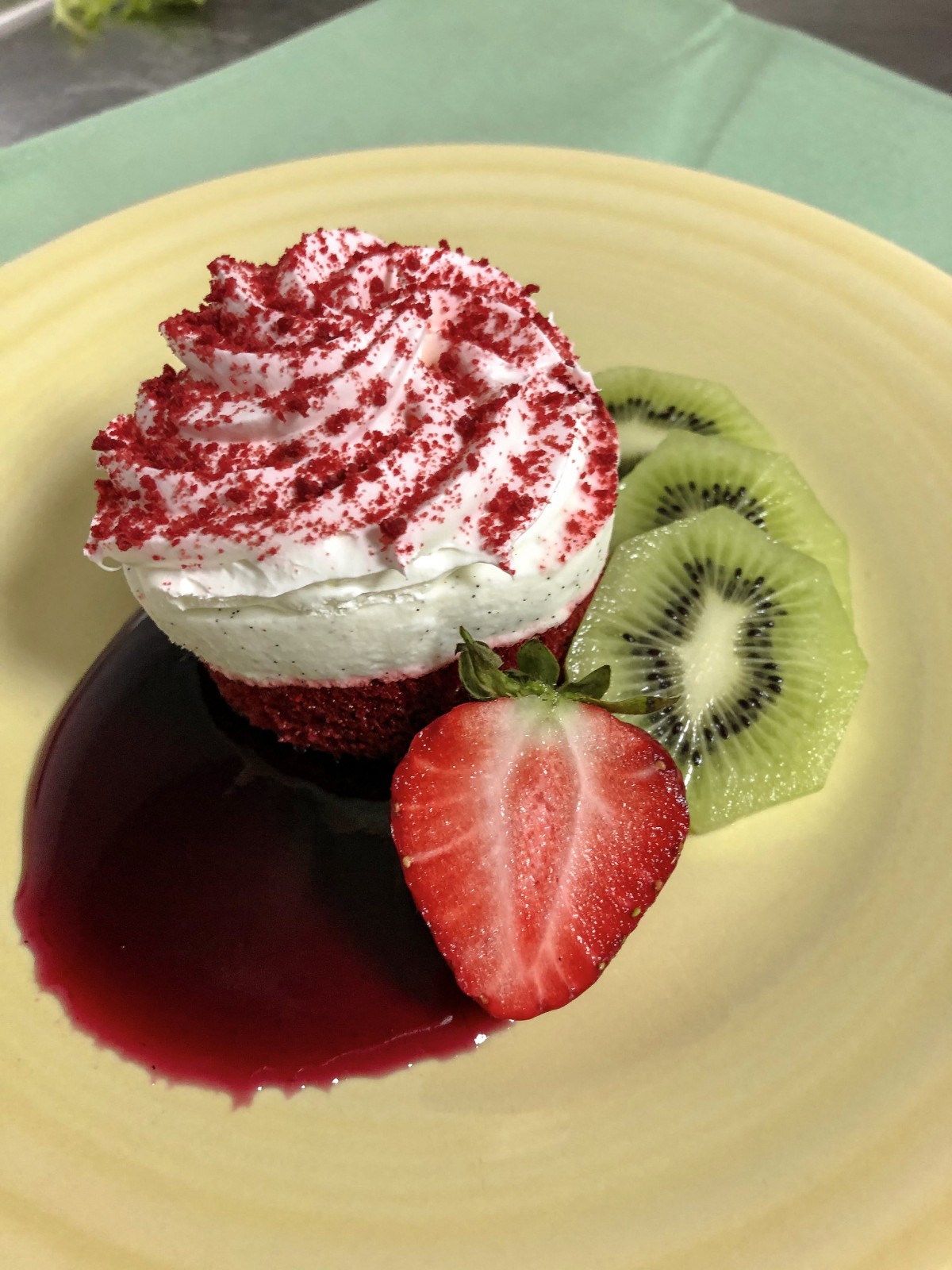 A beautifully decorated cupcake with cream, garnished with fresh slices of strawberry and kiwi.