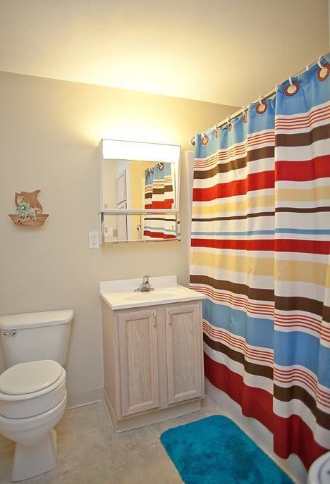 A bright bathroom featuring a colorful striped shower curtain, a sink with a mirror above it, and a toilet.