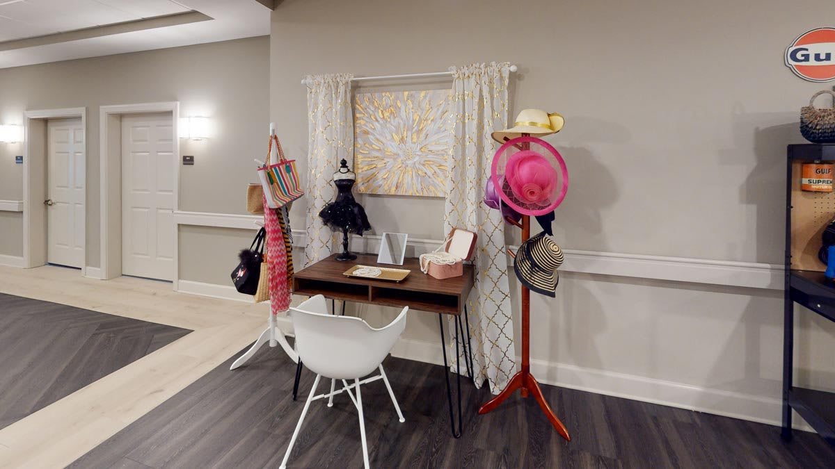 A cozy interior corner with a desk, chair, and decorated coatrack displaying various hats and accessories.