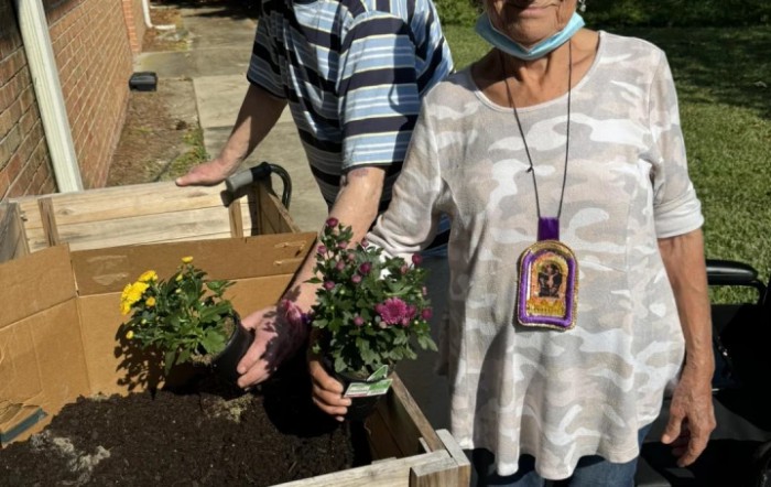 Two people planting flowers in a garden bed outdoors.