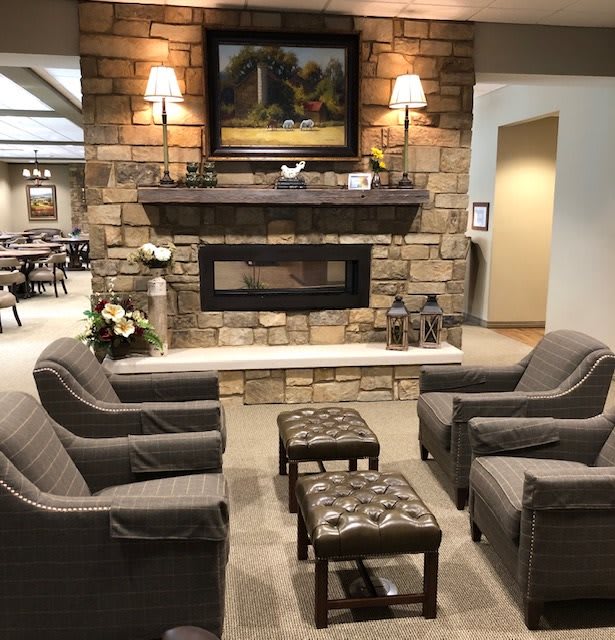 A cozy living room with comfortable armchairs surrounding a stone fireplace, adorned with a decorative painting and soft lighting.