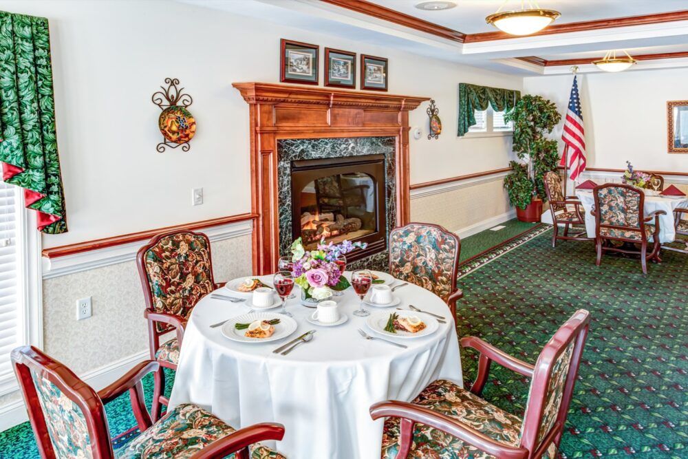 An elegantly decorated dining room with a round table set for a meal, featuring a cozy fireplace and tasteful decor.