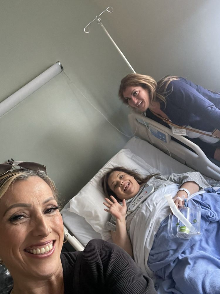 Three women smiling, with one lying in a hospital bed.