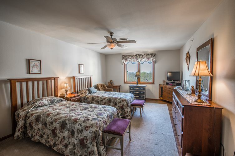 A cozy bedroom with twin beds, a ceiling fan, and a window view.