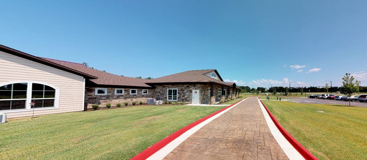 A modern single-story building with a stone facade surrounded by a green lawn and clear blue sky.