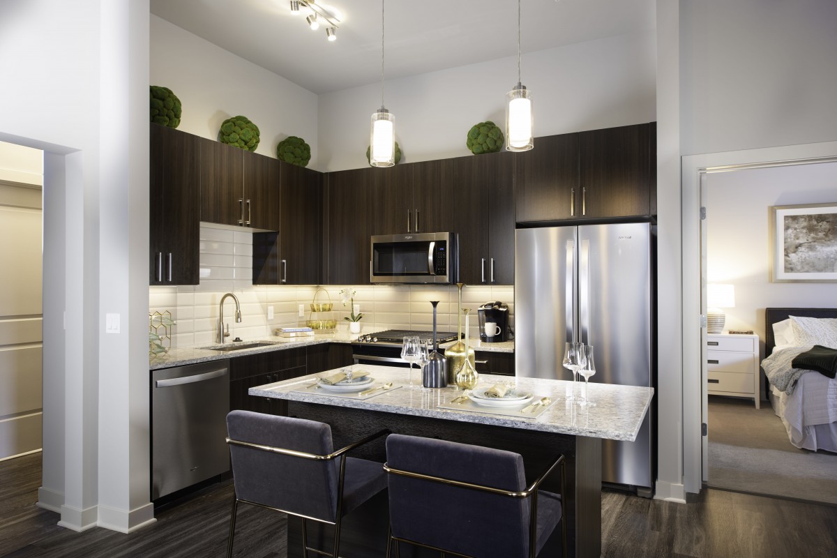 A modern kitchen with dark cabinets, stainless steel appliances, and an island countertop illuminated by pendant lighting.