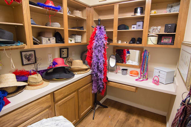 A closet corner filled with colorful hats and accessories, featuring a feather boa and a vanity mirror.