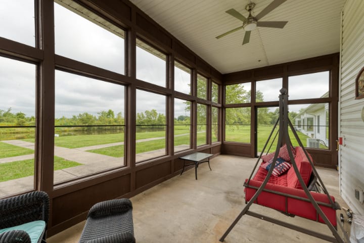 A cozy sunroom with large windows, featuring a red swing and outdoor views.