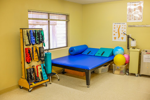 A well-equipped therapy room featuring a blue mat, exercise balls, and various physical therapy tools.