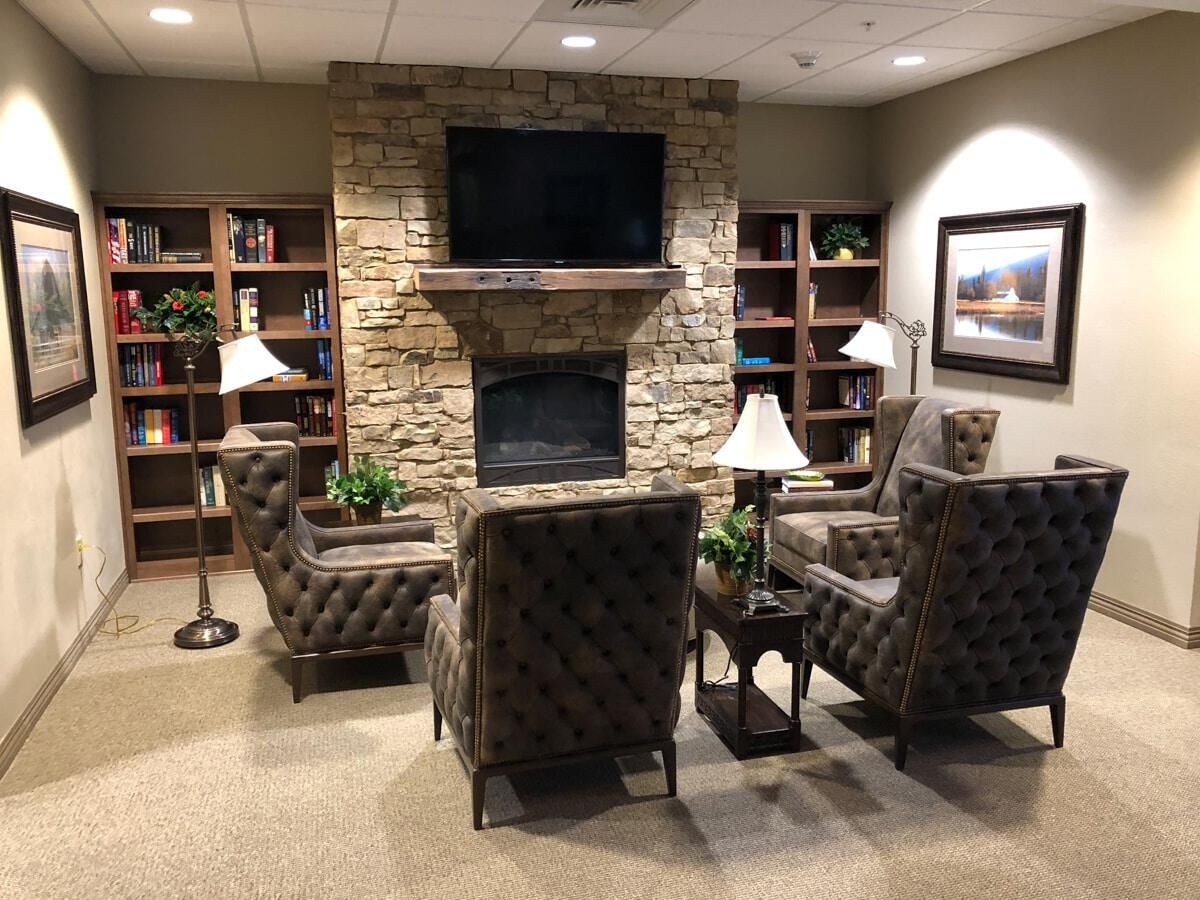 A cozy living room with a stone fireplace, surrounded by bookshelves and elegant chairs.
