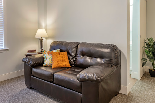 A cozy living room setup featuring a black leather couch adorned with an orange pillow, accompanied by a lamp for soft lighting.