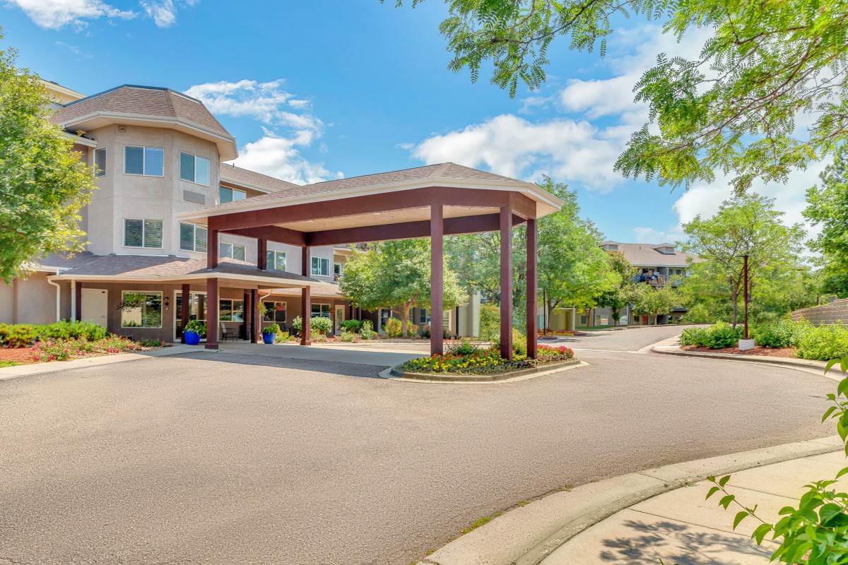 A welcoming entrance to a senior living community surrounded by lush greenery and a clear blue sky.