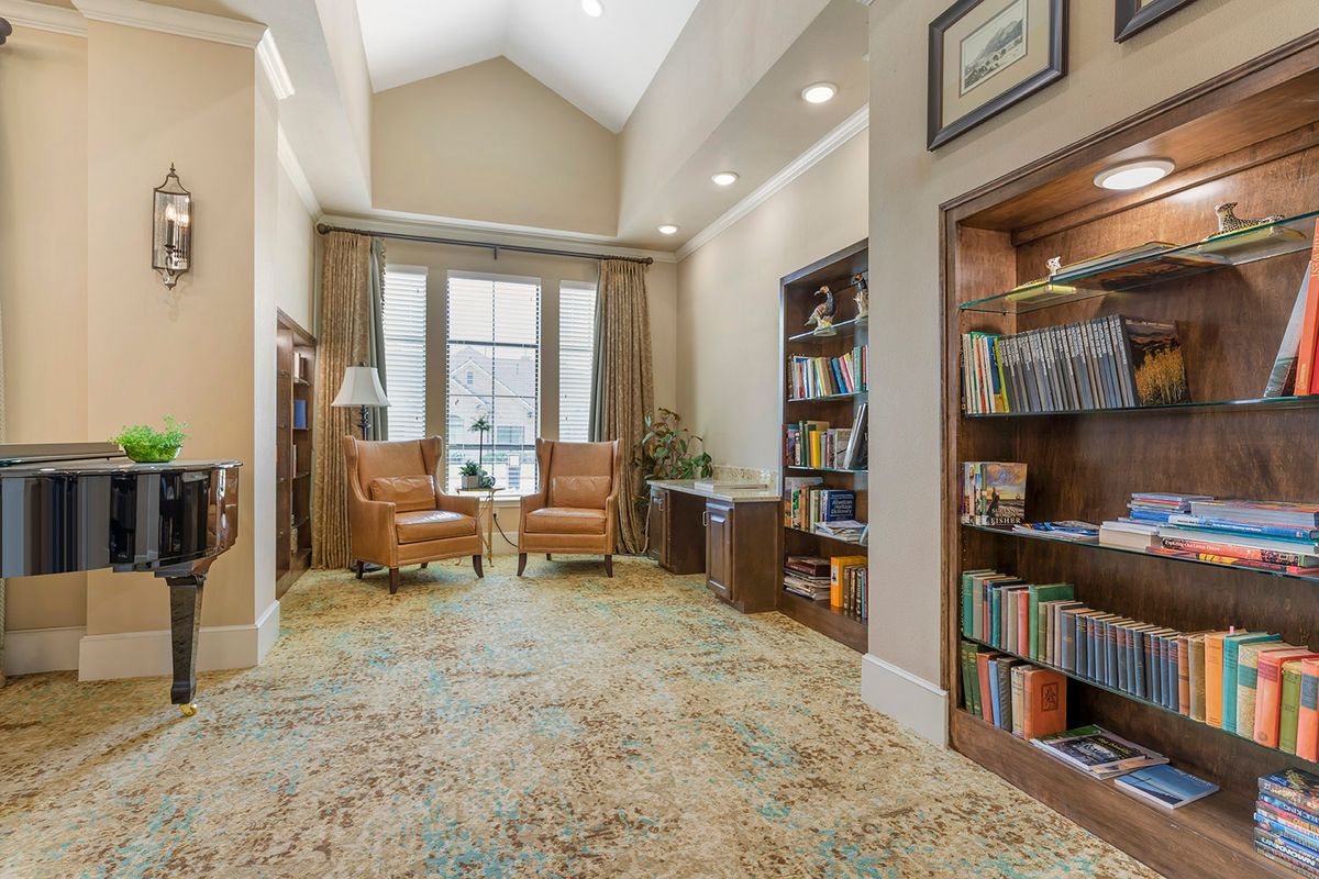 A cozy library setting with bookshelves, comfortable chairs, and large windows.