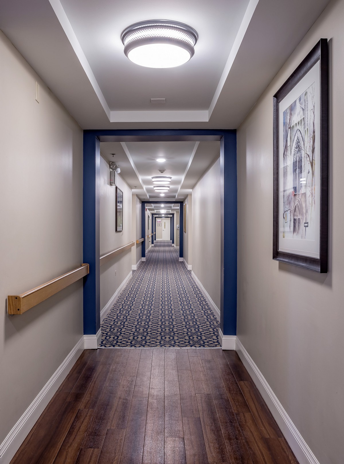 A hotel hallway with patterned carpet and framed artwork.