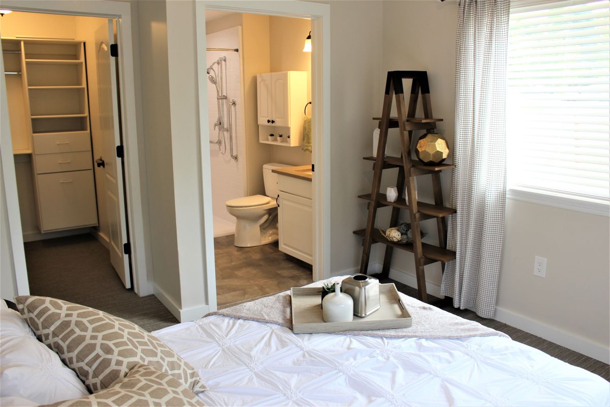 A cozy bedroom with a view into a bathroom, featuring a decorative ladder shelf and a tray on the bed.