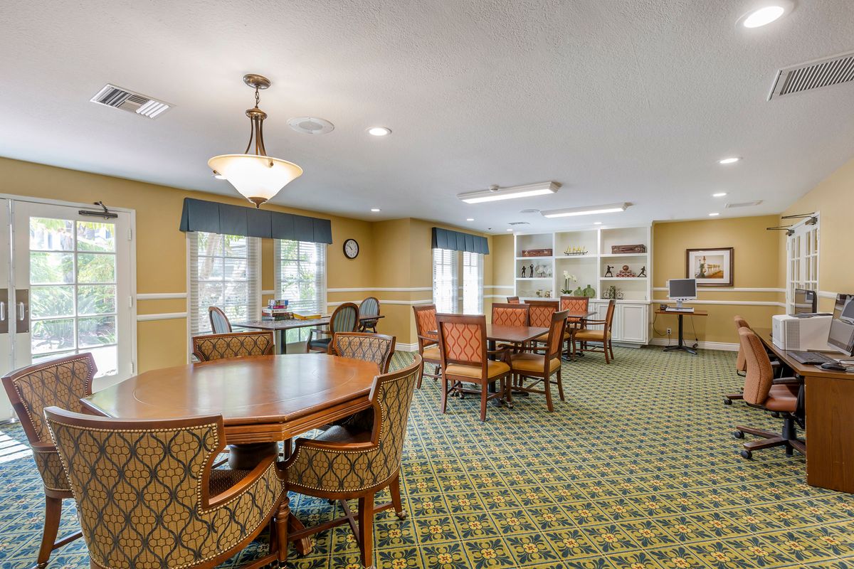 A spacious dining room with multiple tables and chairs, featuring large windows, bookshelves, and elegant lighting.