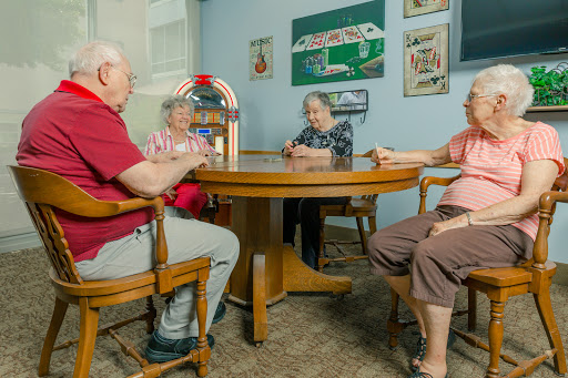 A group of seniors enjoying each other's company around a table with a juke box in a cozy indoor space.