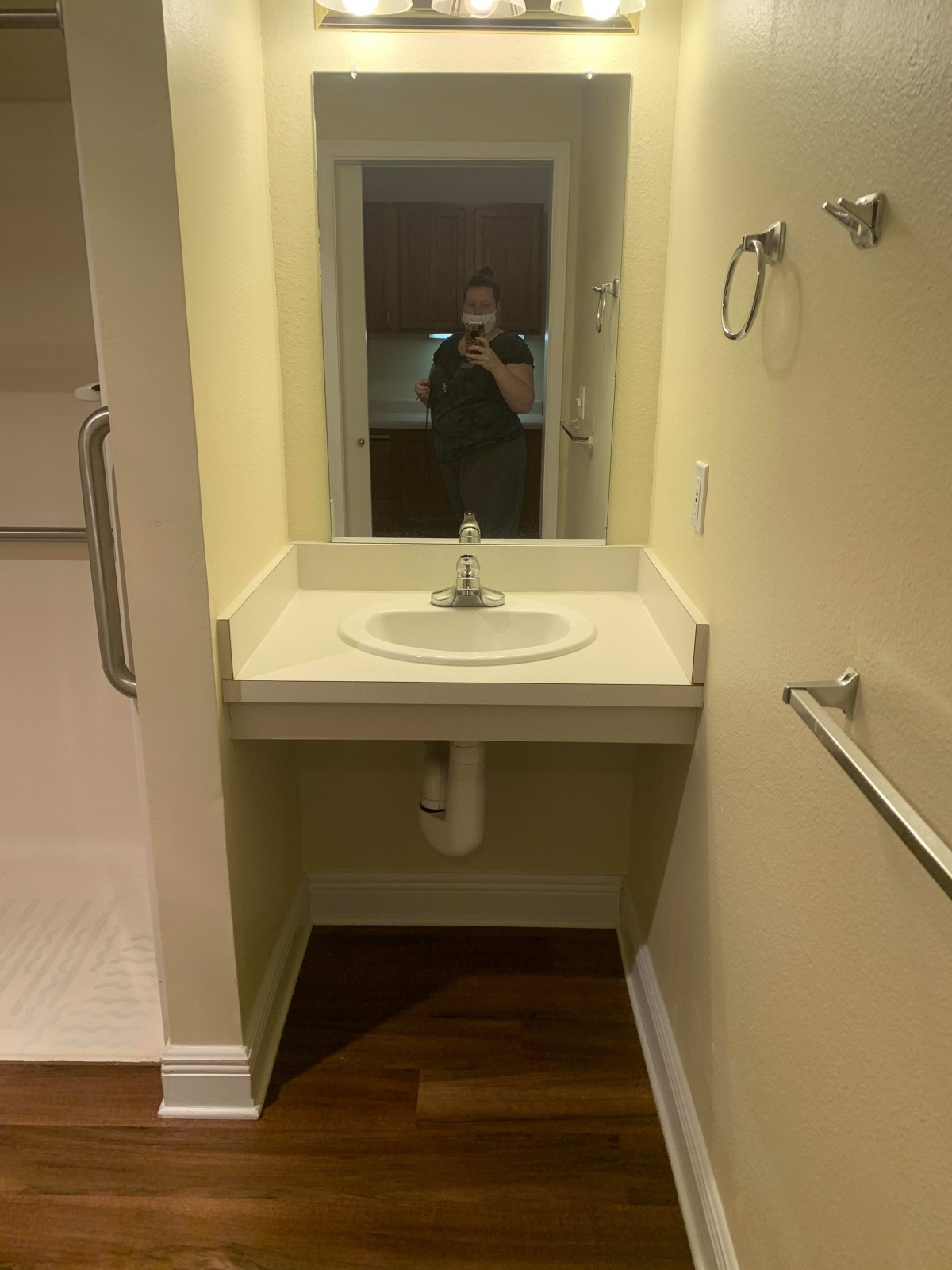 A small bathroom area featuring a wall-mounted sink and a mirror, with a person visible in the reflection.
