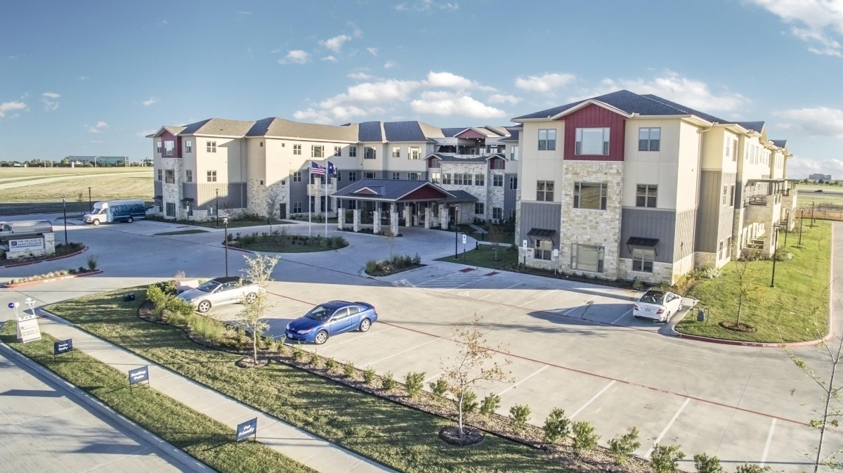 A modern apartment complex with a spacious parking lot and landscaped surroundings under a clear blue sky.