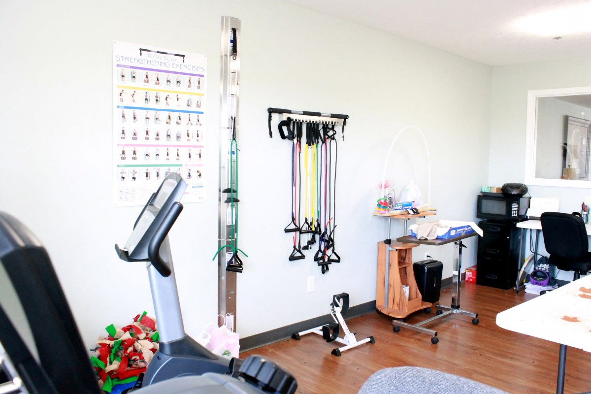 A fitness room equipped with a stationary bike, resistance bands, and other therapy tools.