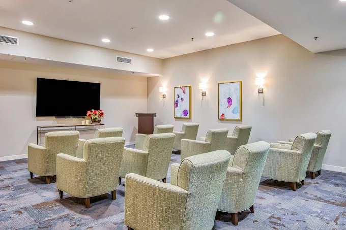 A modern conference room setup with comfortable chairs facing a large television and podium, decorated with artwork on the walls.