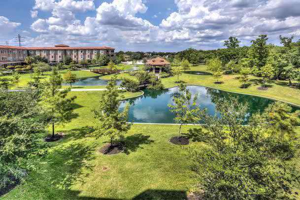 A scenic view of landscaped grounds featuring ponds, trees, and a nearby building under a cloudy sky.