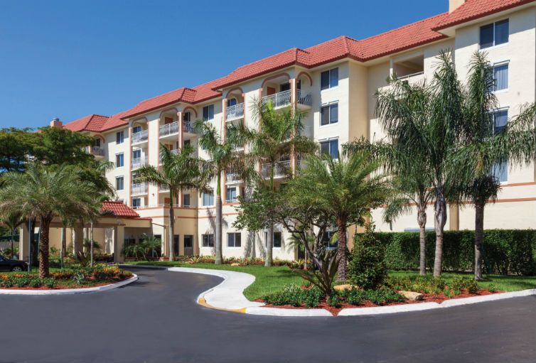A modern apartment building with well-maintained landscaping and palm trees on a sunny day.